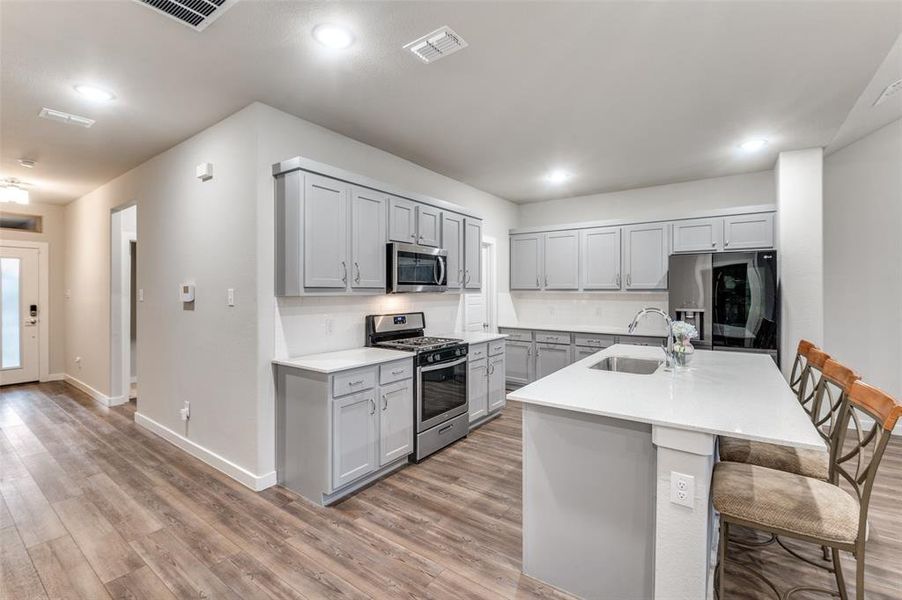 Kitchen featuring a breakfast bar area, gray cabinets, stainless steel appliances, light hardwood / wood-style floors, and sink