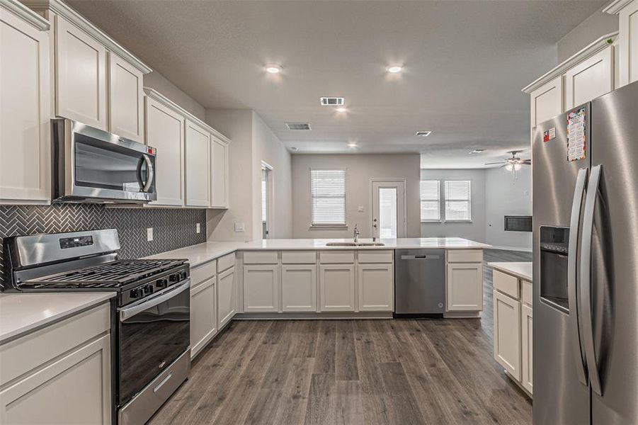 Kitchen featuring tasteful backsplash, kitchen peninsula, hardwood / wood-style floors, and stainless steel appliances