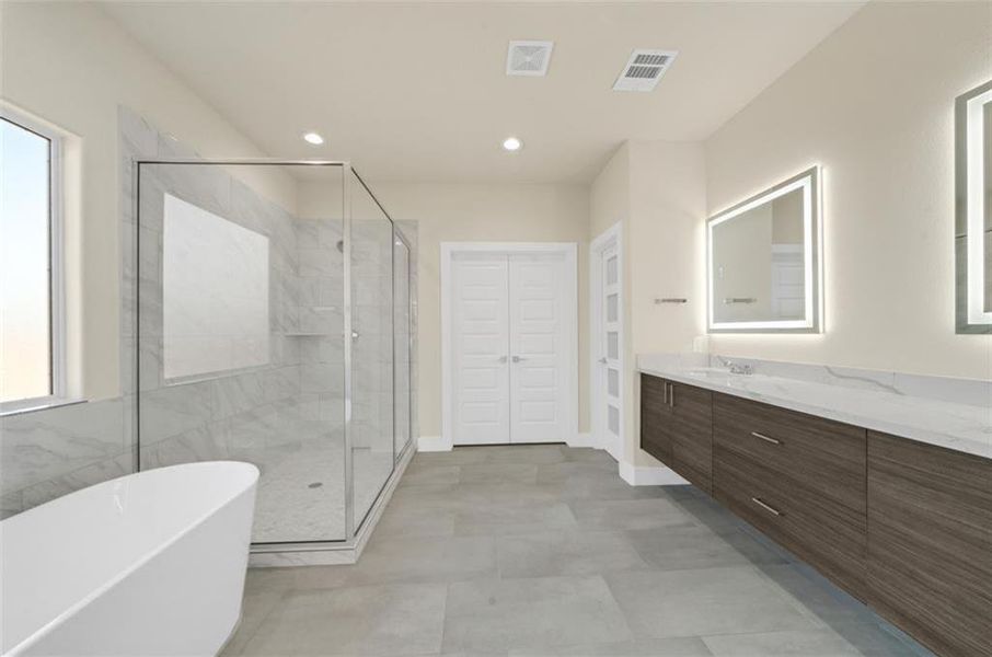 Spacious tiled primary bath with modern soaking tub, double wide comfort shower, rectangular vanity mirrors with LED insert lighting, dual vanity sinks with quartz counter and linear wood cabinetry, all very nice.