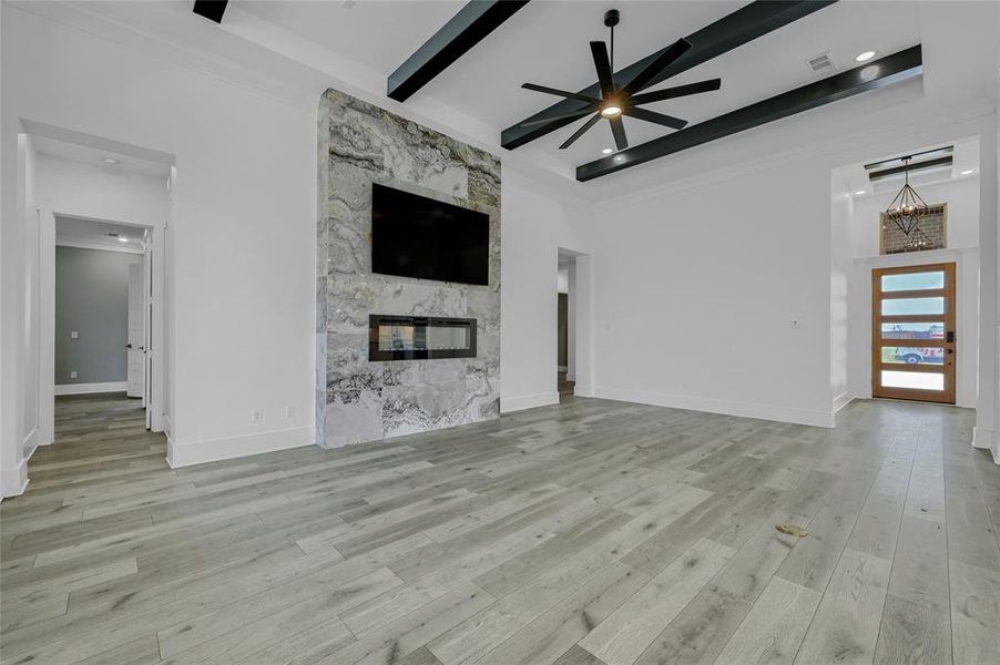 Unfurnished living room with a premium fireplace, ceiling fan, light LVP flooring, and beam ceiling