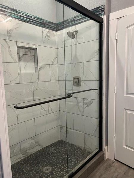 Bathroom featuring a shower with shower door and wood-type flooring
