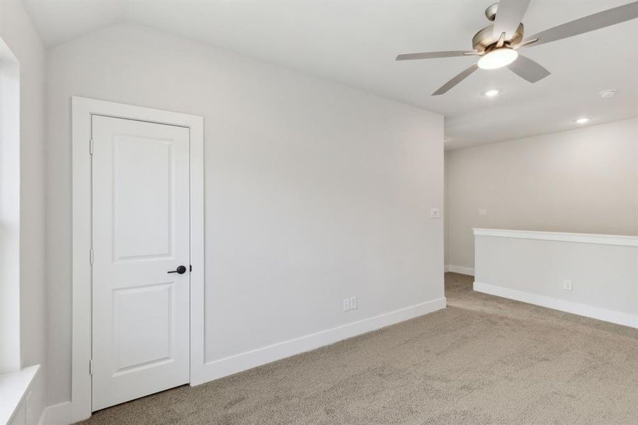 Empty room with light colored carpet, ceiling fan, and vaulted ceiling