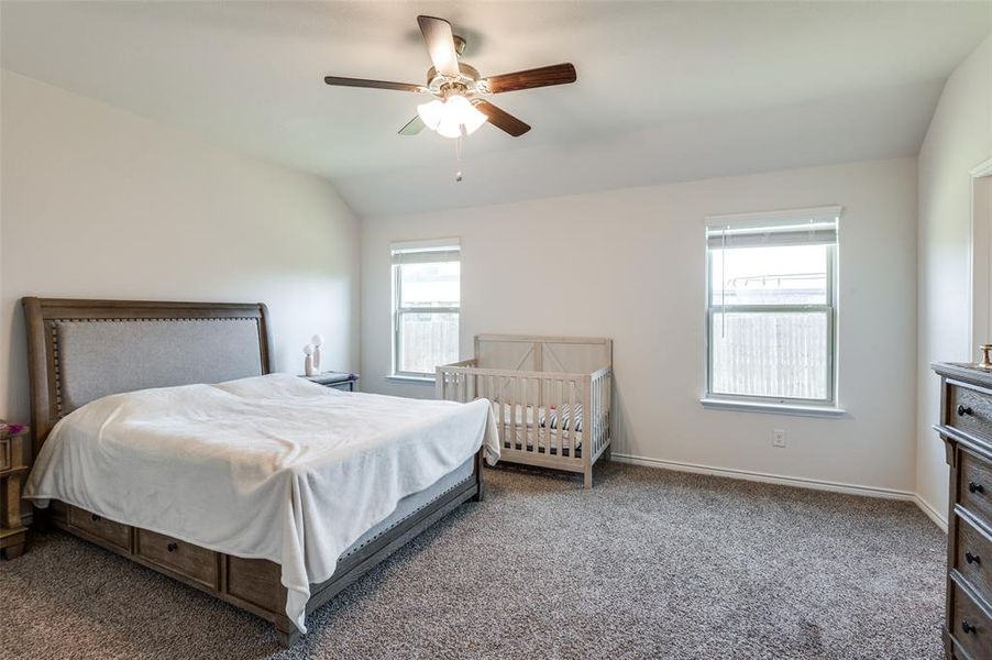 Bedroom featuring ceiling fan, multiple windows, carpet flooring, and lofted ceiling