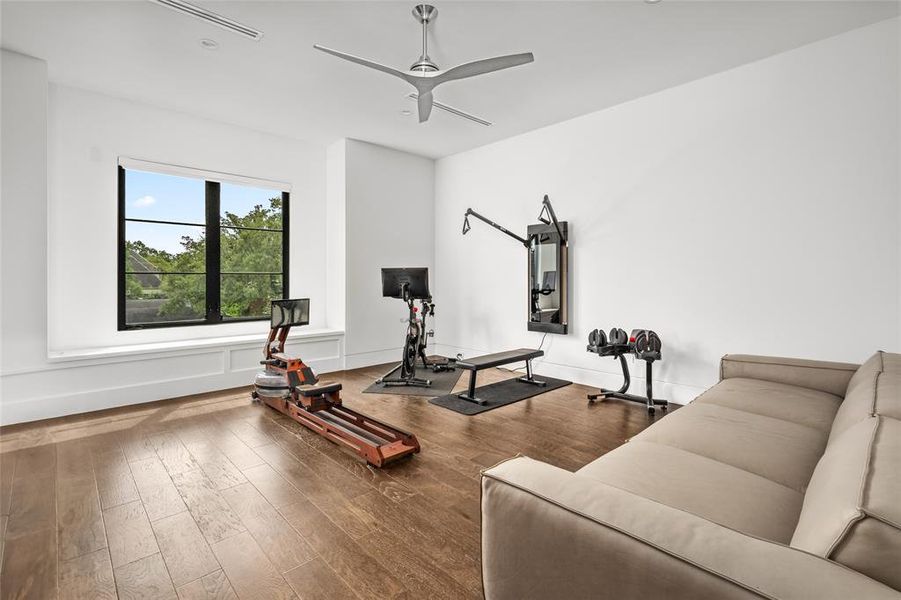 Currently being used as a home gym, this spacious secondary bedroom features large windows that provide ample natural light, dark hardwood flooring, and a modern ceiling fan for comfort.