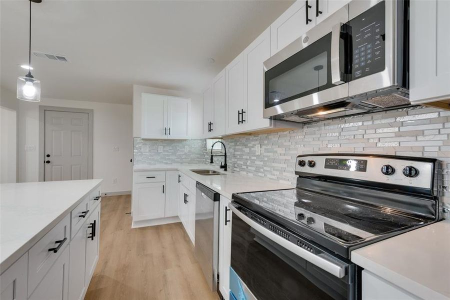 Kitchen with backsplash, light wood-type flooring, white cabinetry, and appliances with stainless steel finishes