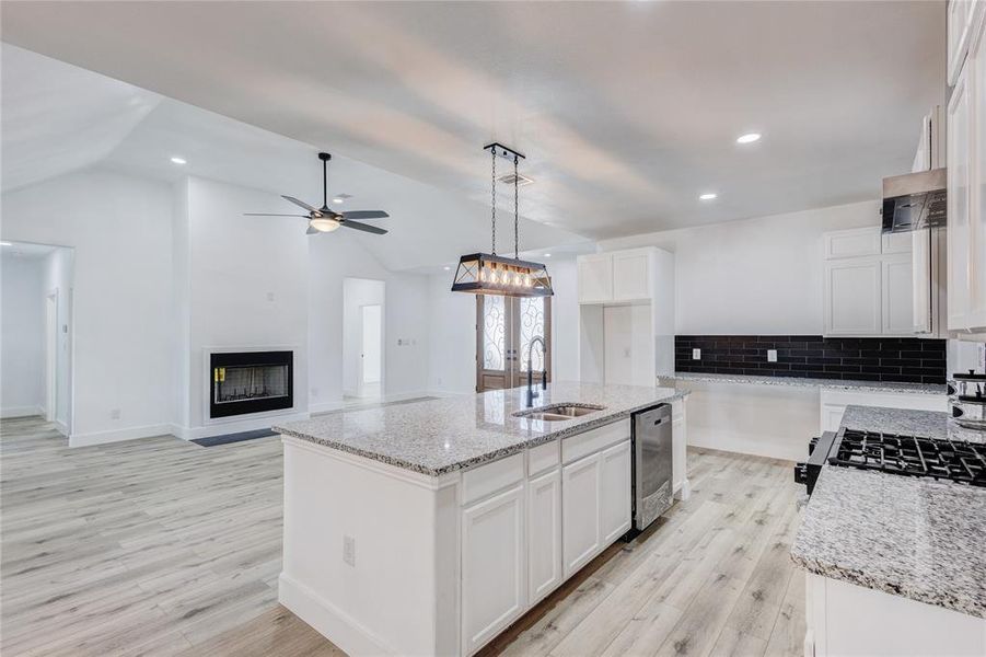 Kitchen with an island with sink, hanging light fixtures, white cabinetry, vaulted ceiling, and dishwasher