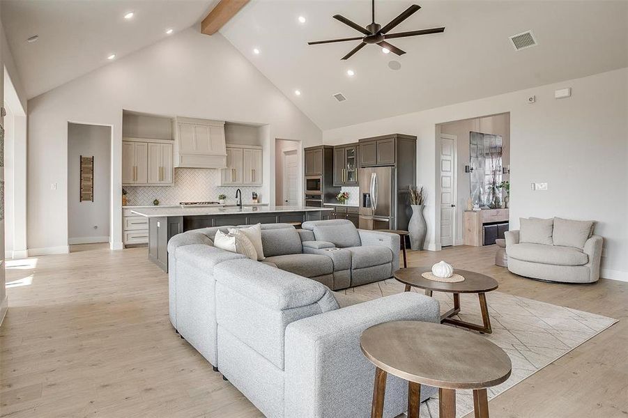 Living room featuring beamed ceiling, sink, light wood-type flooring, high vaulted ceiling, and ceiling fan