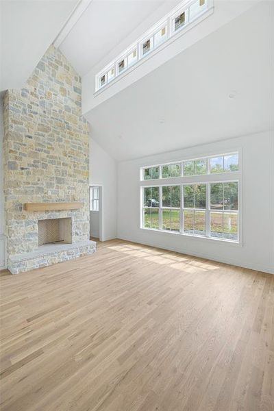 Unfurnished living room with light hardwood / wood-style flooring, high vaulted ceiling, beam ceiling, and a fireplace