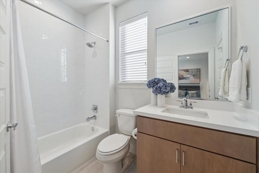 This ensuite bathroom, connected to the third-floor bedroom, features a full bath and shower combination with contemporary tile. The spacious vanity provides plenty of counter space, and the window adds natural light, creating a bright and refreshing atmosphere.