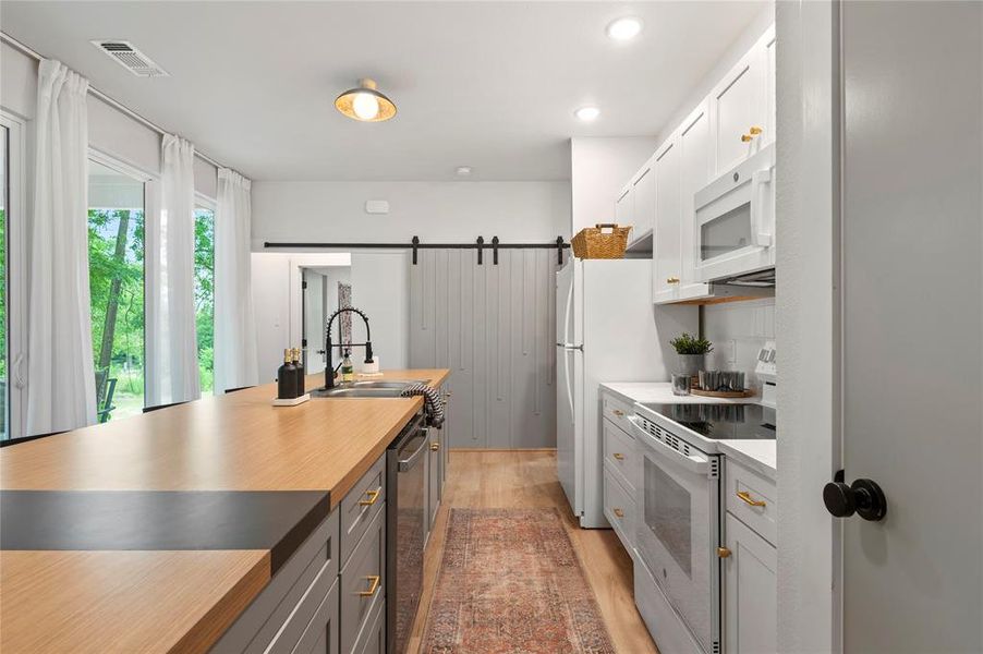 Kitchen featuring white cabinetry, wooden counters, white appliances, sink, and light hardwood / wood-style flooring. Large, walk-in pantry through door to the right, extends behind the stairs.