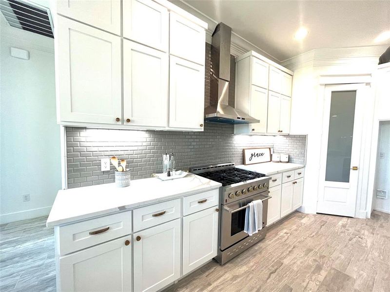 Kitchen featuring white cabinetry, light hardwood / wood-style flooring, tasteful backsplash, wall chimney range hood, and high end stainless steel range oven