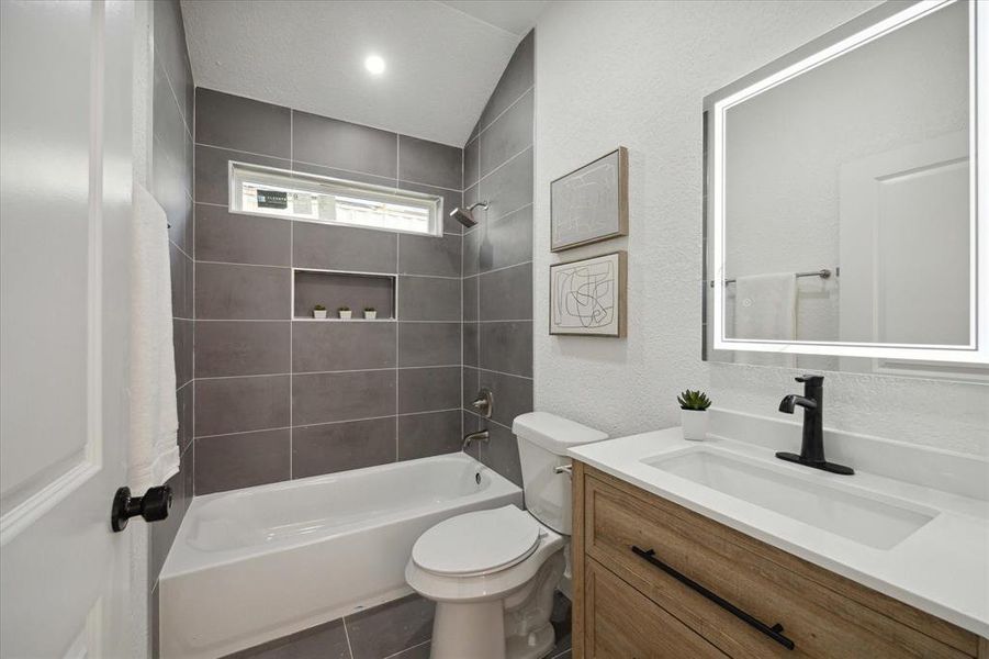 A second full bathroom features a contemporary vanity with a lit mirror above. Also notice the crisp modern tile that extends from the floor through the tub/shower enclosure.