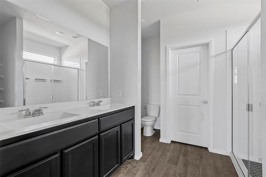 Bathroom with a shower with door, a textured ceiling, wood-type flooring, vanity, and toilet