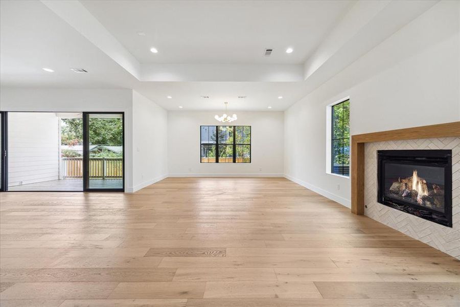 Looking from the family room into the formal dining room, you'll find a space defined by engineered white oak flooring and illuminated by a designer gold and glass globe chandelier. The room is adorned with designer neutral paint and recessed LED lighting, with windows offering northern and western exposures.