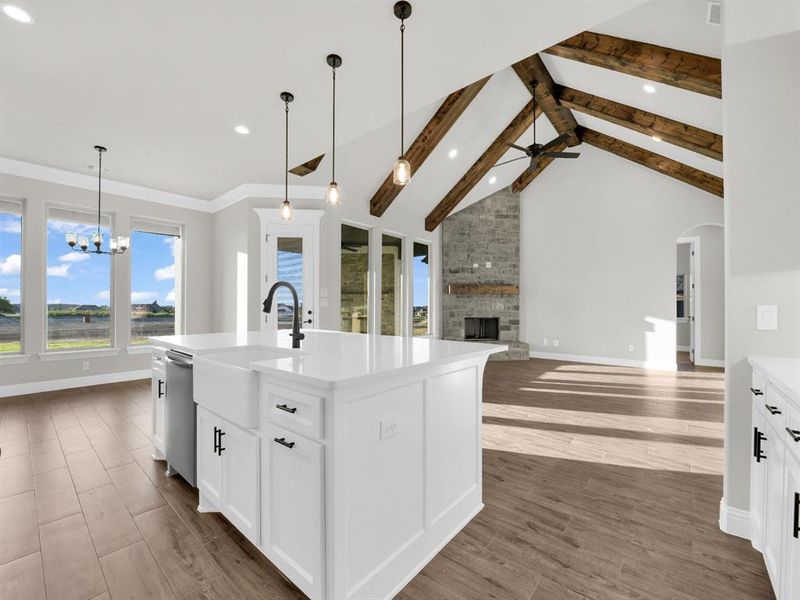 Kitchen featuring a fireplace, ceiling fan with notable chandelier, a kitchen island with sink, beam ceiling, and white cabinets