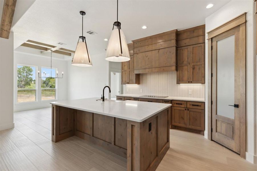 Kitchen with hanging light fixtures, decorative backsplash, light wood-type flooring, sink, and a center island with sink