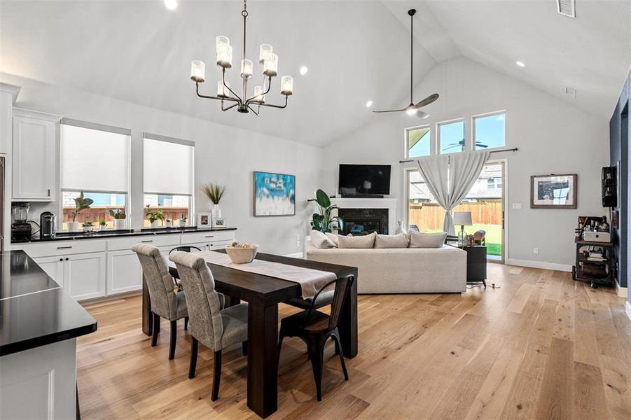 Dining area featuring a high end fireplace, high vaulted ceiling, light hardwood / wood-style floors, and ceiling fan with notable chandelier