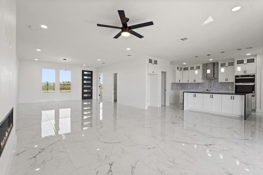 Kitchen with white cabinetry, decorative light fixtures, decorative backsplash, ceiling fan, and wall chimney range hood