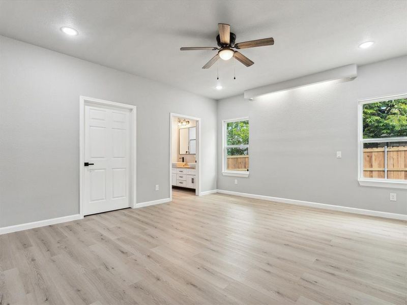 Unfurnished bedroom featuring ceiling fan, ensuite bathroom, and light hardwood / wood-style flooring