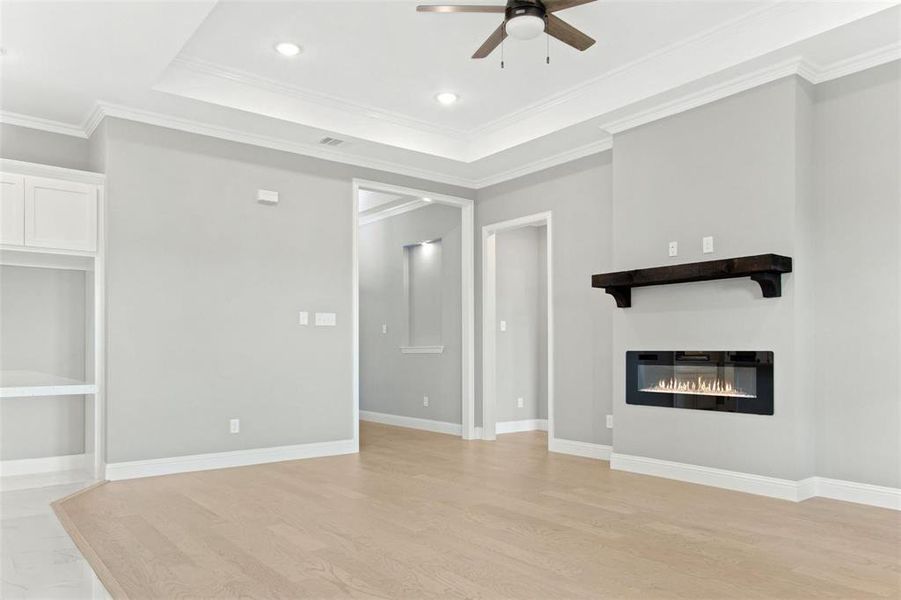 Unfurnished living room with a tray ceiling, ceiling fan, crown molding, and light hardwood / wood-style flooring