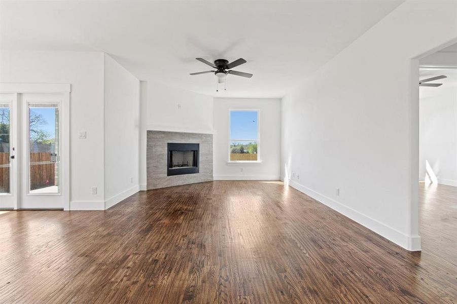 Unfurnished living room with a tiled fireplace, dark wood-type flooring, and ceiling fan