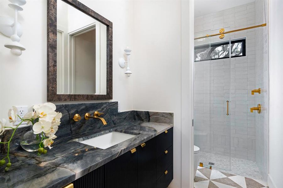 The first floor guest bathroom was designed to wow! The Ijen Blue countertop and sumptuous deep navy high-sheen lacquered cabinetry are offset with bright brass hardware and plumbing and a striking patterned marble floor.