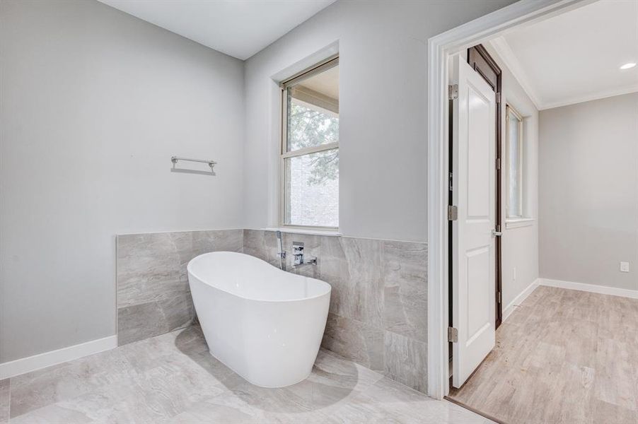 Bathroom featuring tile walls, wood-type flooring, ornamental molding, and a tub