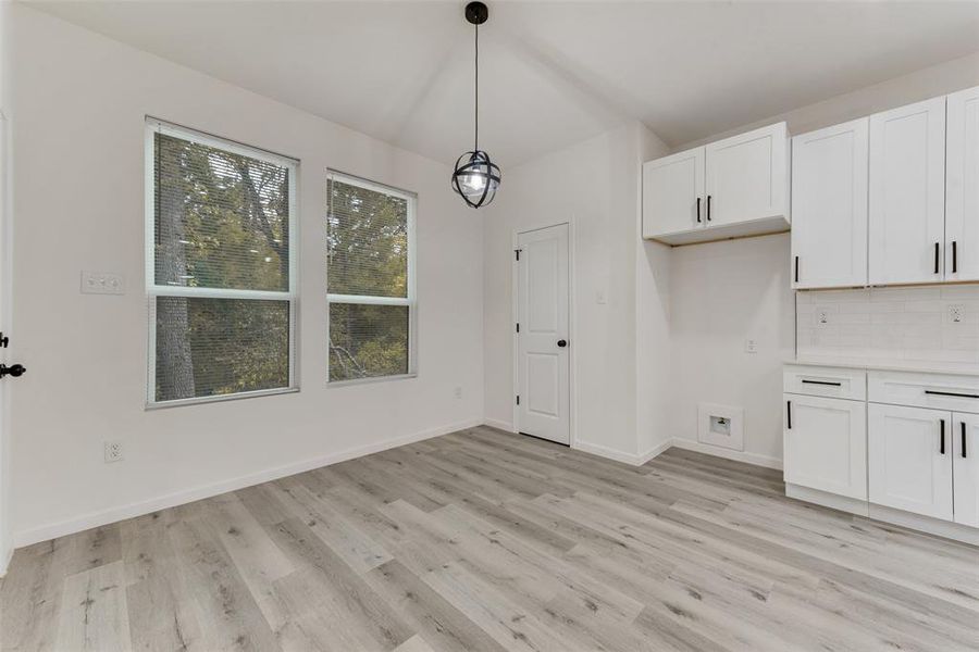 Kitchen featuring decorative backsplash, white cabinetry, light hardwood / wood-style flooring, and decorative light fixtures