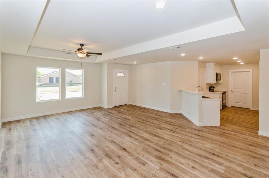 Unfurnished living room with light wood-type flooring, a raised ceiling, sink, and ceiling fan