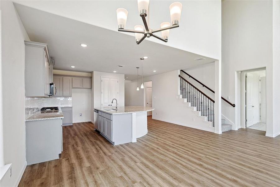 Kitchen featuring sink, hanging light fixtures, gray cabinets, light hardwood / wood-style flooring, and a center island with sink