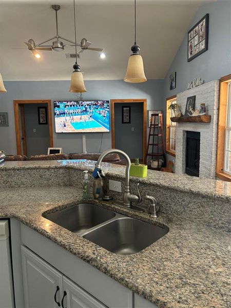 Kitchen with a fireplace, hanging light fixtures, sink, lofted ceiling, and ceiling fan