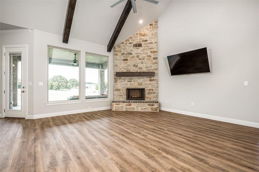 Unfurnished living room featuring beamed ceiling, hardwood / wood-style floors, a fireplace, high vaulted ceiling, and ceiling fan