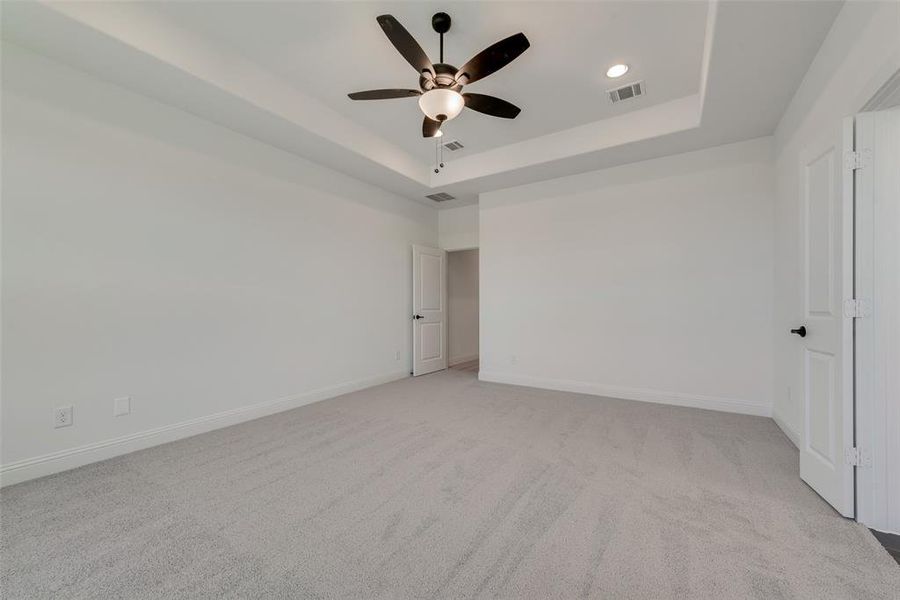 Empty room with carpet, ceiling fan, and a tray ceiling