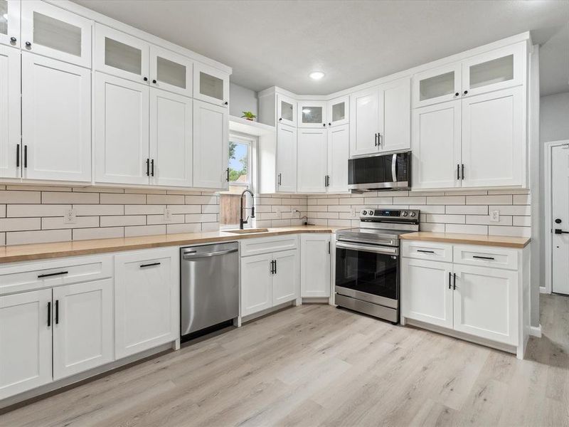 Kitchen with white cabinetry, light hardwood / wood-style flooring, butcher block countertops, sink, and appliances with stainless steel finishes