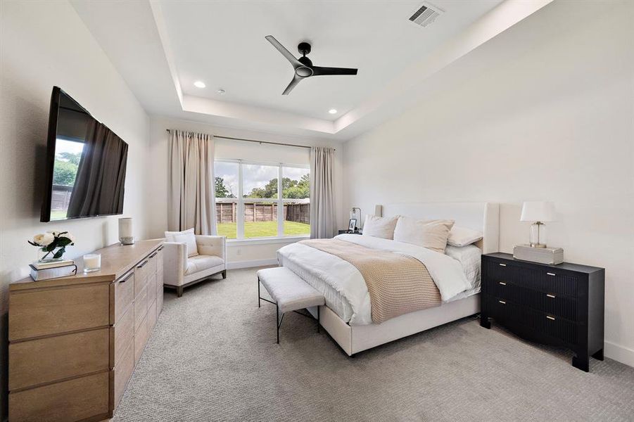 A primary bedroom graced with tray ceilings and a captivating view.