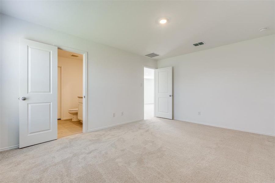 Unfurnished bedroom with ensuite bathroom and light carpet