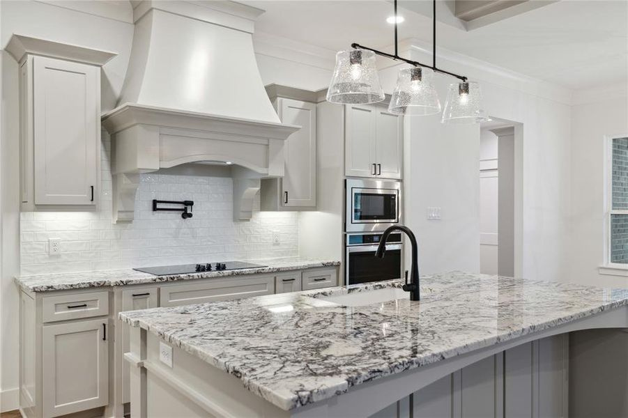 Kitchen with decorative light fixtures, custom exhaust hood, stainless steel appliances, crown molding, and backsplash