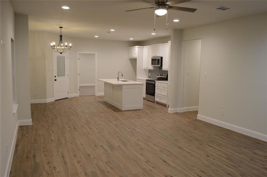 Kitchen island with sink, white cabinetry, and stainless steel appliances