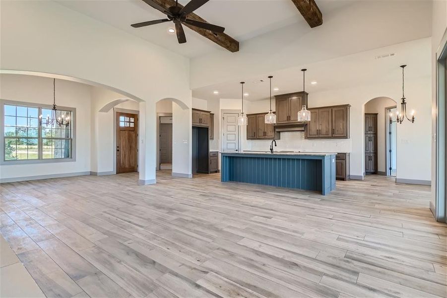 Kitchen with ceiling fan with notable chandelier, pendant lighting, beamed ceiling, light hardwood / wood-style floors, and a kitchen island with sink