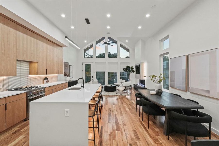 Kitchen featuring stainless steel stove, light hardwood / wood-style floors, a kitchen breakfast bar, high vaulted ceiling, and a kitchen island with sink