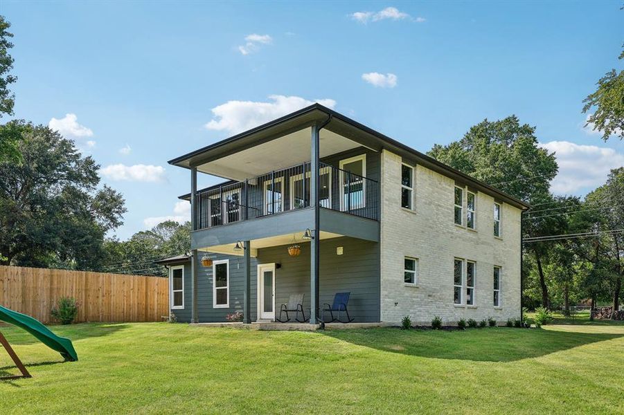 Rear view of house featuring a balcony and a yard