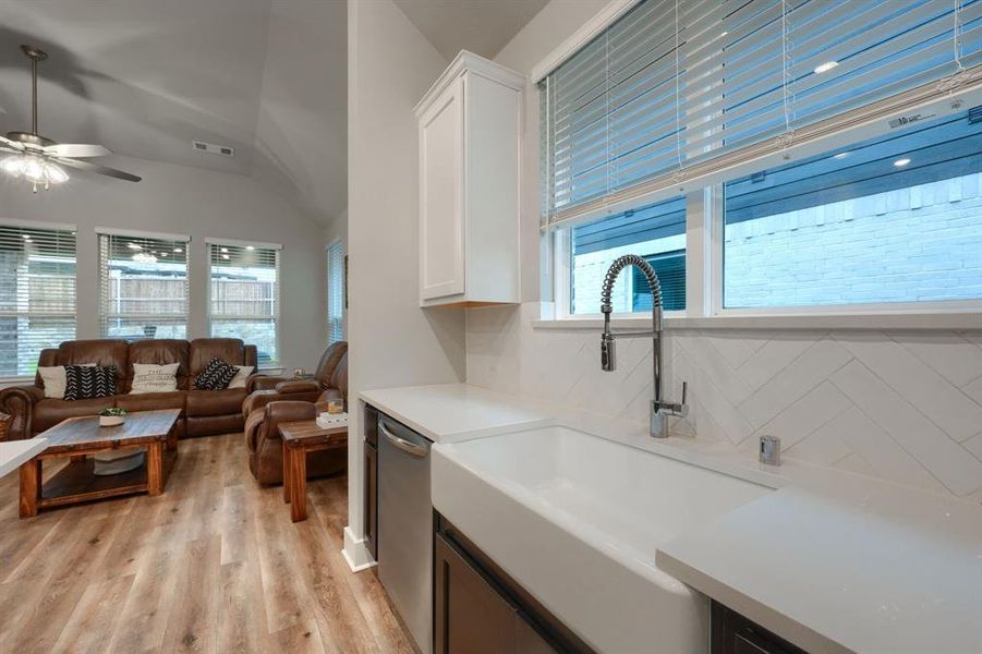 Kitchen with ceiling fan, white cabinets, sink, light wood-type flooring, and vaulted ceiling