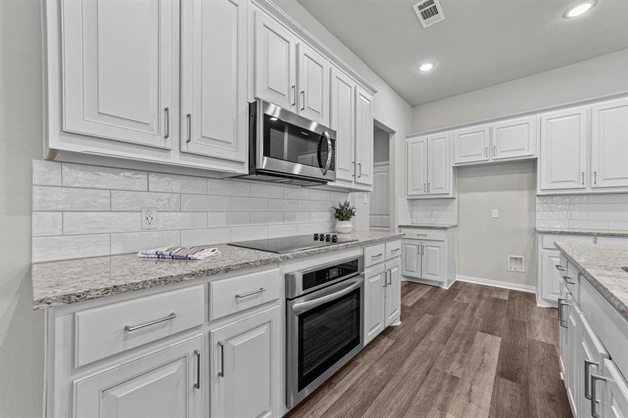 Kitchen with white cabinetry, tasteful backsplash, stainless steel appliances, wood-type flooring, and light stone countertops