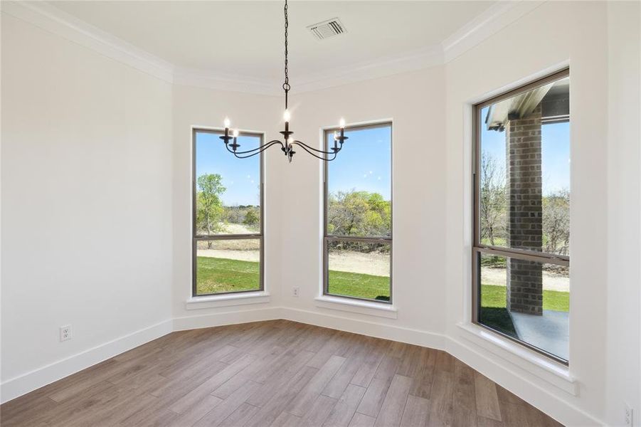 Unfurnished dining area featuring an inviting chandelier, crown molding, hardwood / wood-style flooring, and a healthy amount of sunlight