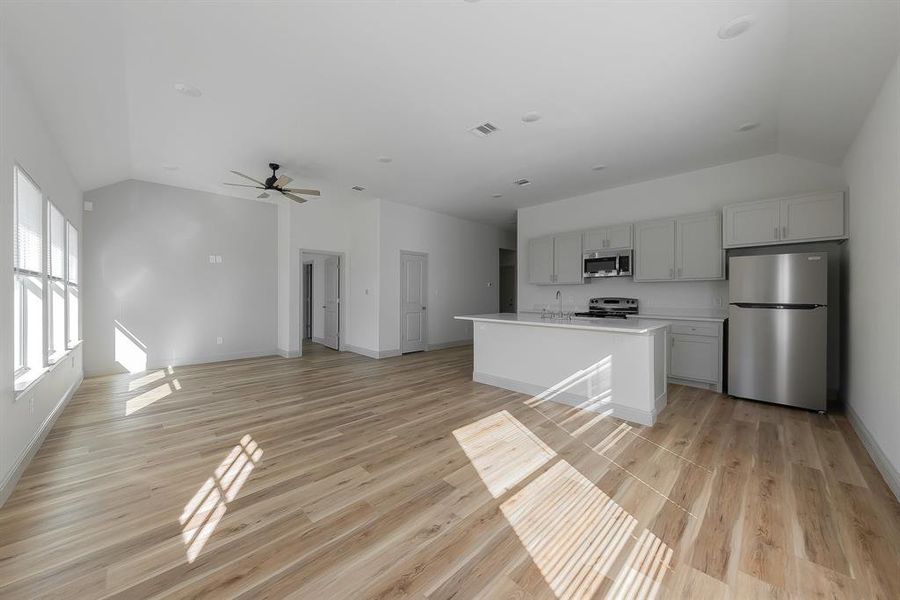 Kitchen with appliances with stainless steel finishes, vaulted ceiling, light hardwood / wood-style flooring, ceiling fan, and a kitchen island with sink