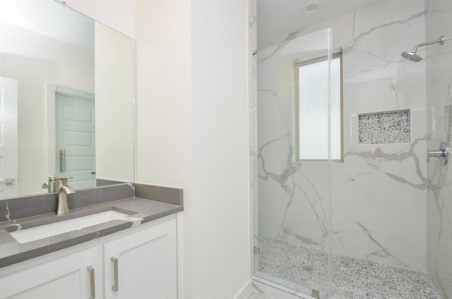 Secondary full bathroom with walk-in shower surrounded by polished porcelain tile walls, single vanity with quartz countertop.