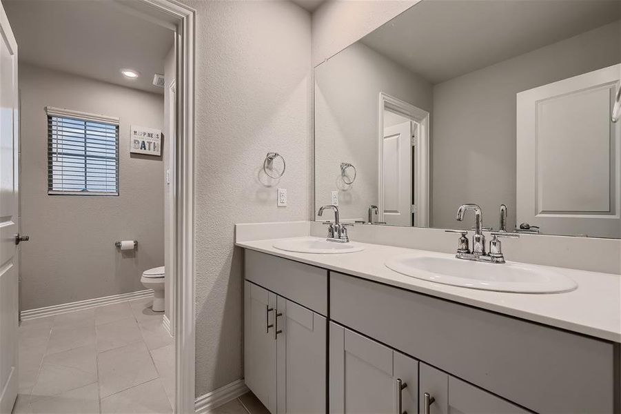 Bathroom with tile floors, dual bowl vanity, and toilet
