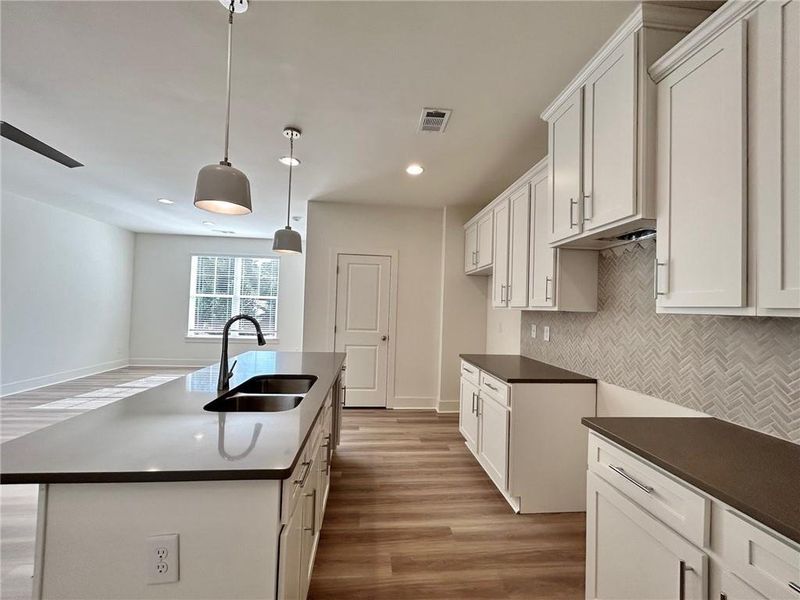 Kitchen with sink, a kitchen island with sink, tasteful backsplash, decorative light fixtures, and hardwood / wood-style floors