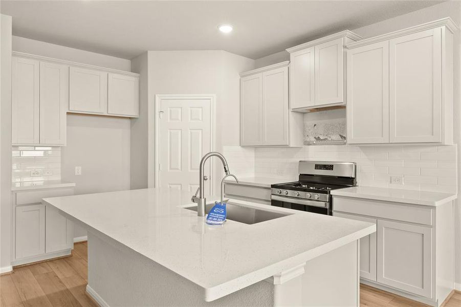 This light and bright kitchen features a large quartz island, white cabinets, a large sink overlooking your family room, recessed lighting, and beautiful backsplash.