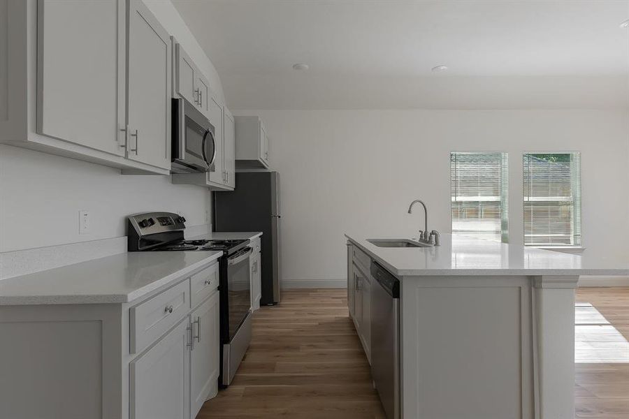 Kitchen with light wood-type flooring, a center island with sink, appliances with stainless steel finishes, and sink